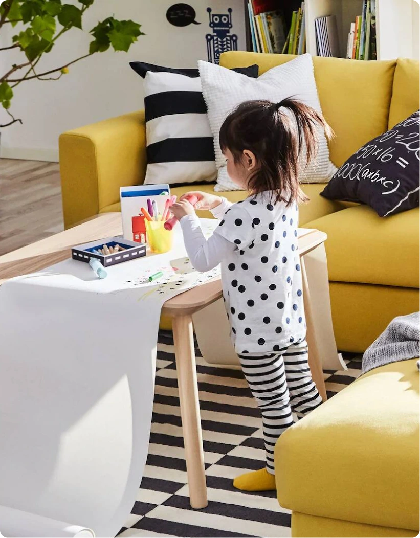 Little girl in a modern UAE home standing in front of a bright yellow couch, showcasing IKEA.ae's playful living room setup highlighting the brand's use of the .ae domain, supported by Gatehills.